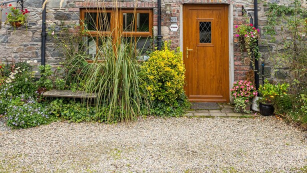 A stone house with a wooden door, two windows, and a gravel driveway. - Priest Bridge Cottage (Newcastle)