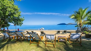 A beachside area with wooden lounge chairs and a table, a clear view of the ocean, and a small boat in the distance. - Loharano Lodge (Nosy Be)