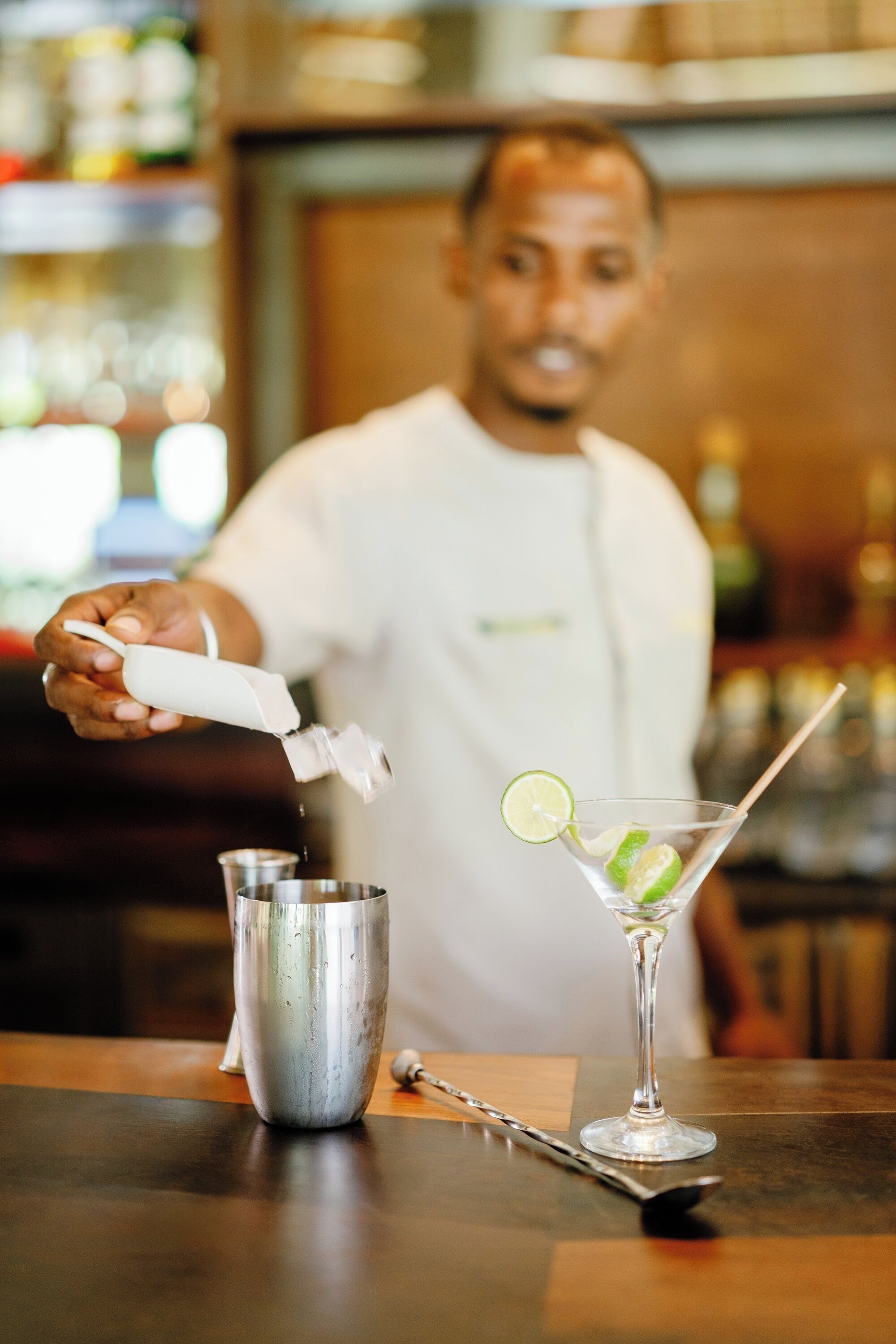 Um bartender preparando uma bebida com um coqueteleira e um copo de martini com um toque de limão.