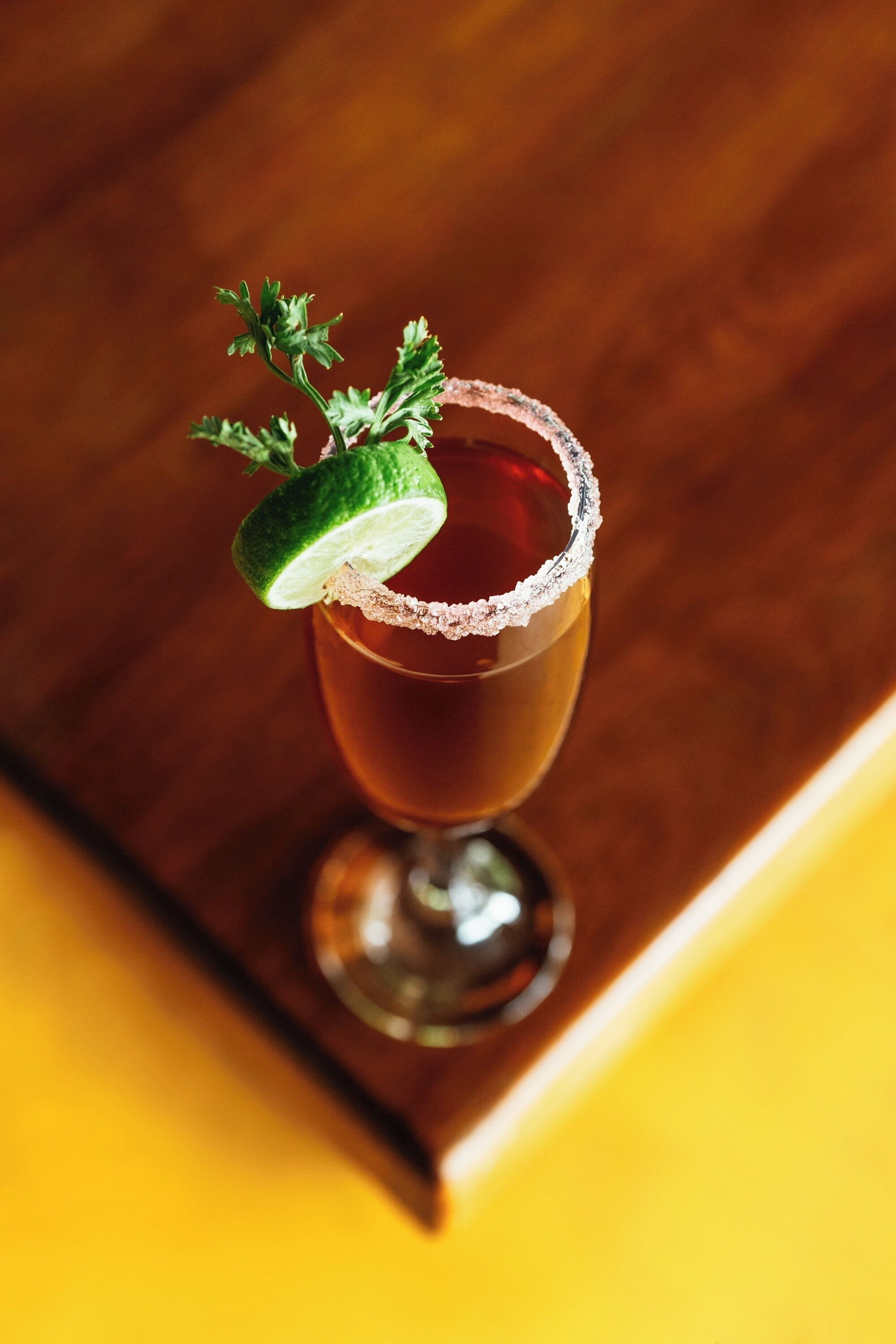 A cocktail glass with a salted rim and a lime garnish on a wooden surface.
