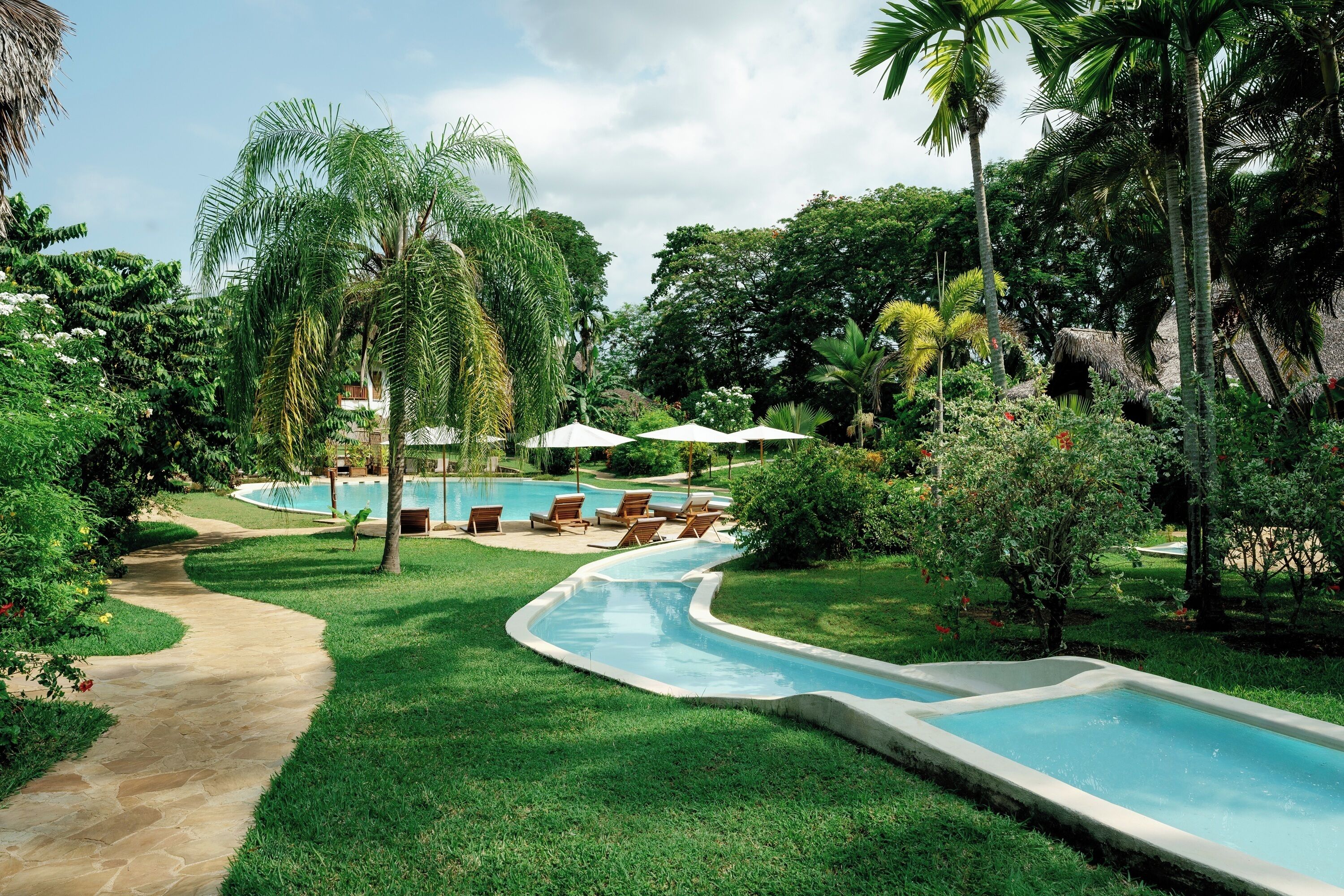 A swimming pool area with a curved pathway, lounge chairs, and palm trees.