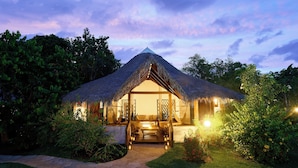A thatched-roof structure with a wooden porch and steps leading to a door, surrounded by lush greenery. - Loharano Lodge (Nosy Be)
