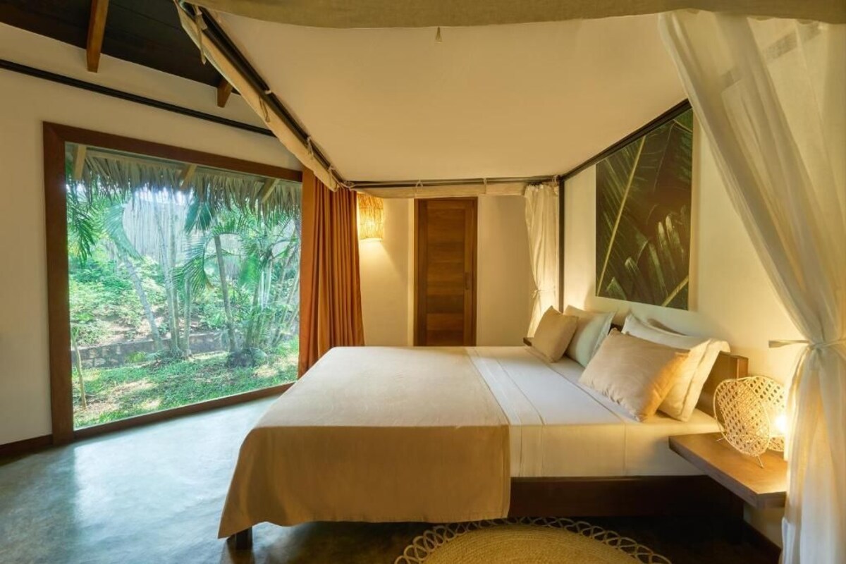 Un dormitorio con una cama grande, vistas al verdor a través de una ventana y un cabecero de madera.