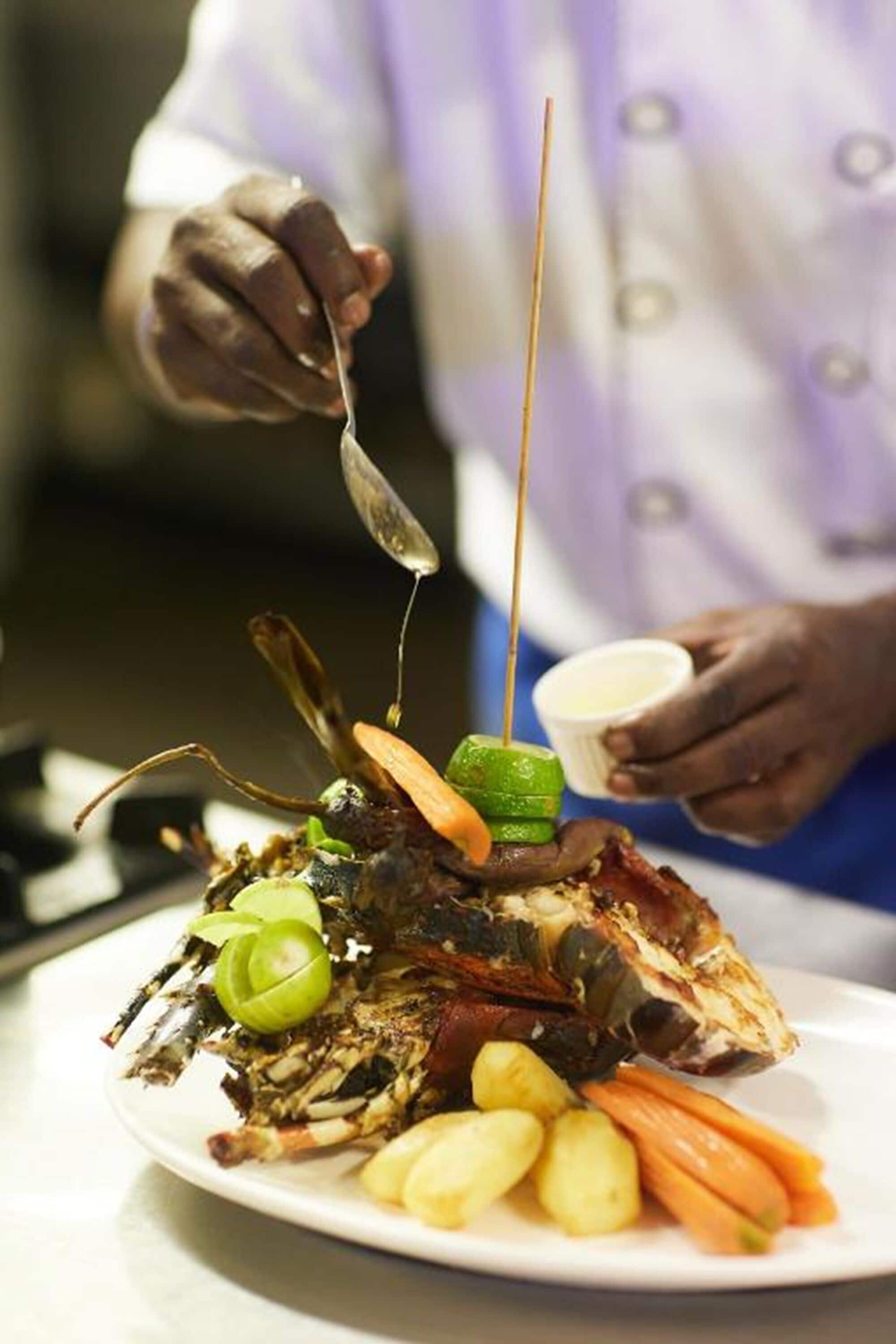 A chef preparing a dish with a lobster tail, lime, and vegetables on a plate.