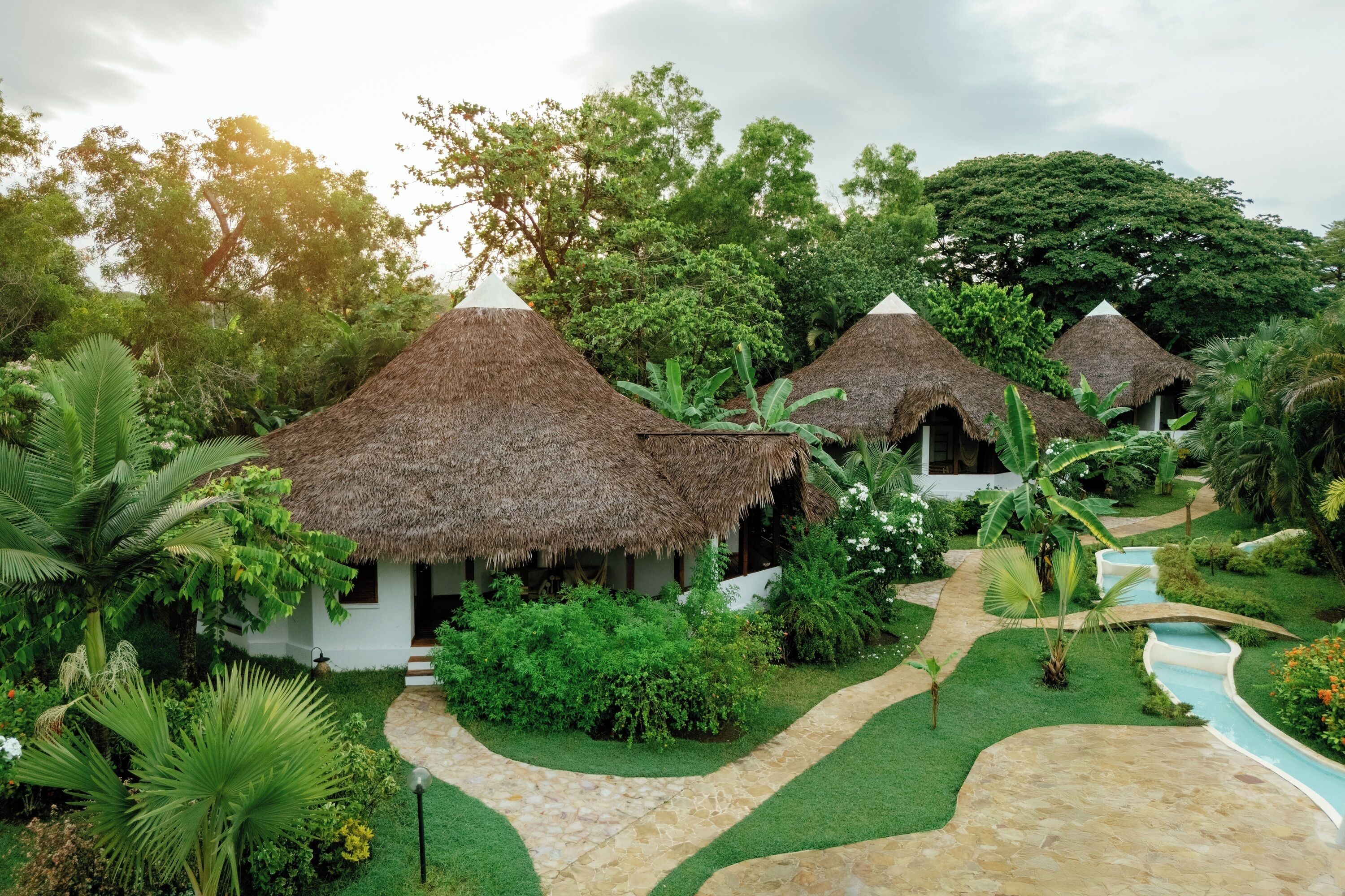 Un complexe hôtelier doté de bungalows aux toits de chaume, d’un sentier pavé de pierres et d’une végétation luxuriante.