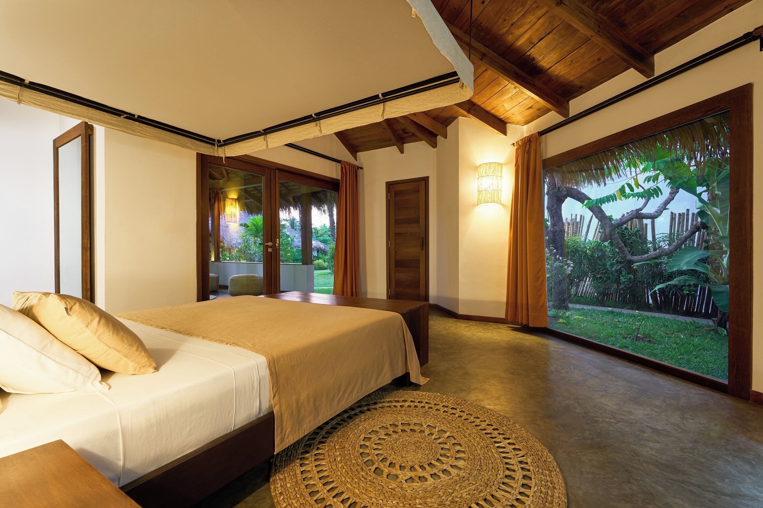 A bedroom with a bed, a large window, and a view of a garden.