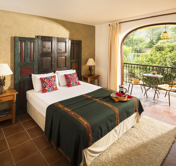 A hotel room with a large bed, a balcony with a table and chairs, and a view of greenery outside. - Hotel Villa Santa Catarina (Santa Catarina Palopo)