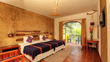 Camera da letto con un letto grande, una testiera in legno, un tavolino con una sedia, una televisione e un balcone con vista sul verde.