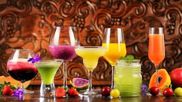 Variedad de bebidas coloridas en distintos vasos, un tarro con líquido verde y algunas frutas como fresas y una pitahaya sobre una mesa de madera.