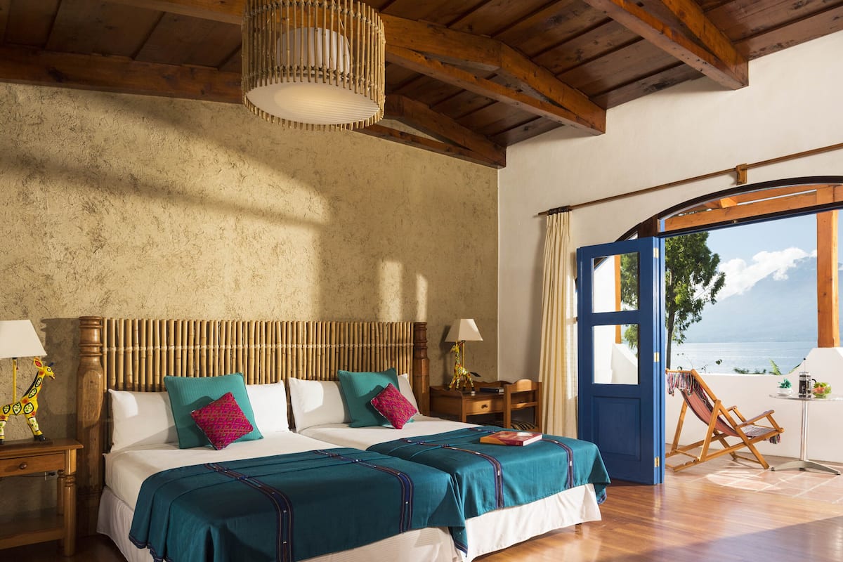 A spacious bedroom with a large bed, wooden ceiling beams, and a view of the sea through an open door.