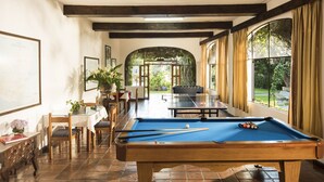 Une table de billard dans une pièce qui comprend un coin repas, une carte accrochée au mur et de grandes fenêtres.