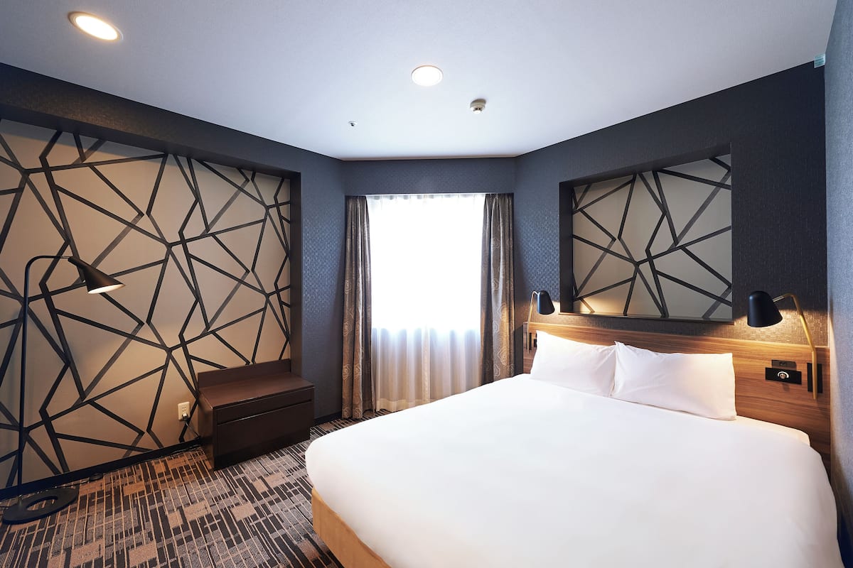 A modern hotel room with a large bed, a nightstand, a desk, and a decorative wall with geometric patterns.