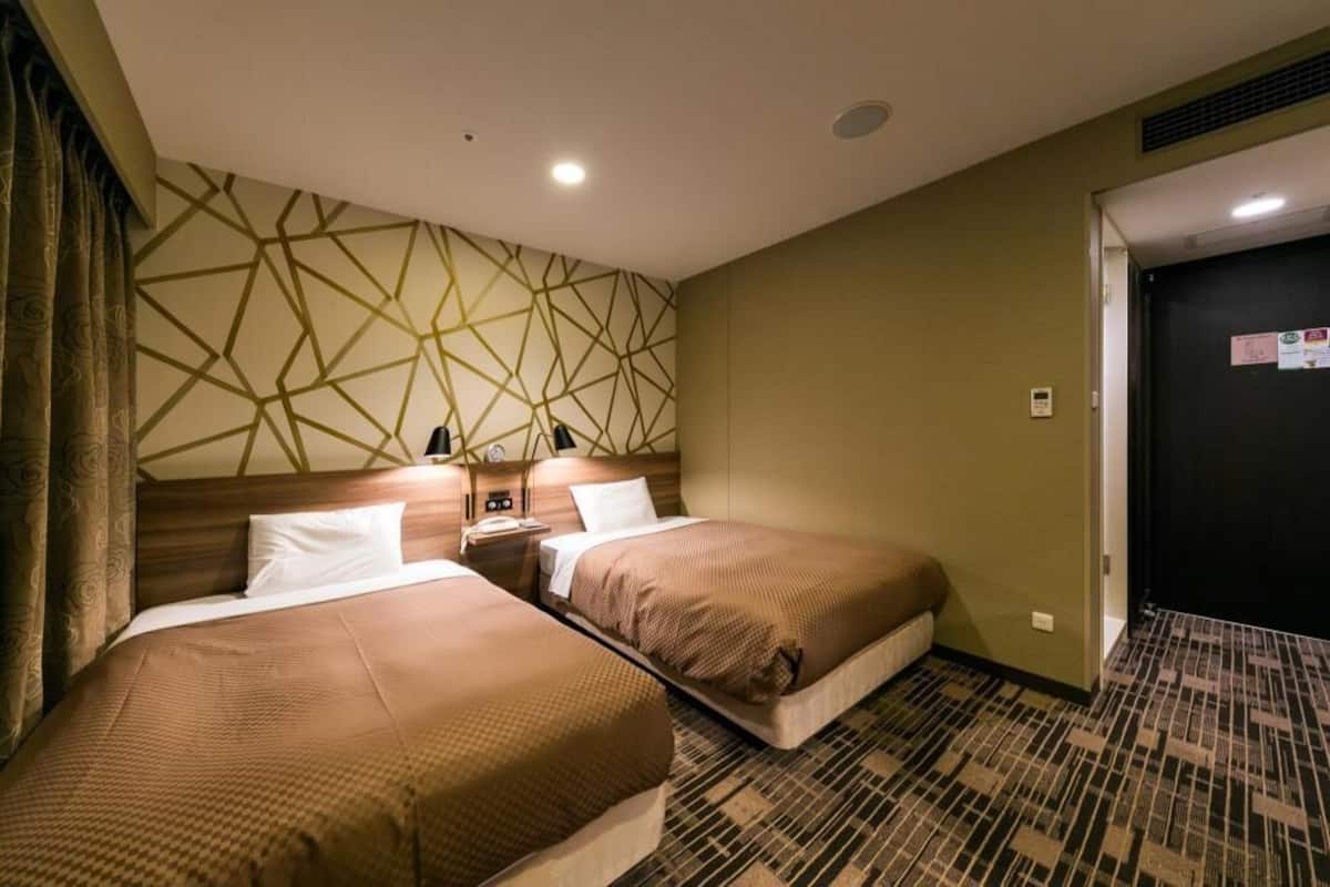 A hotel room with two beds, a geometric patterned wall, a door, and a carpeted floor.