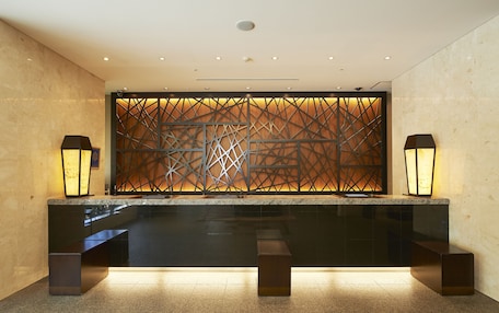 A reception area with a modern design, featuring a reception desk, two standing lamps, and a decorative wall with geometric patterns.