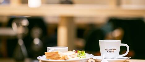 Una mesa con un plato de sándwiches, una taza de café y una taza que dice 'EXCELSIOR CAFE'.