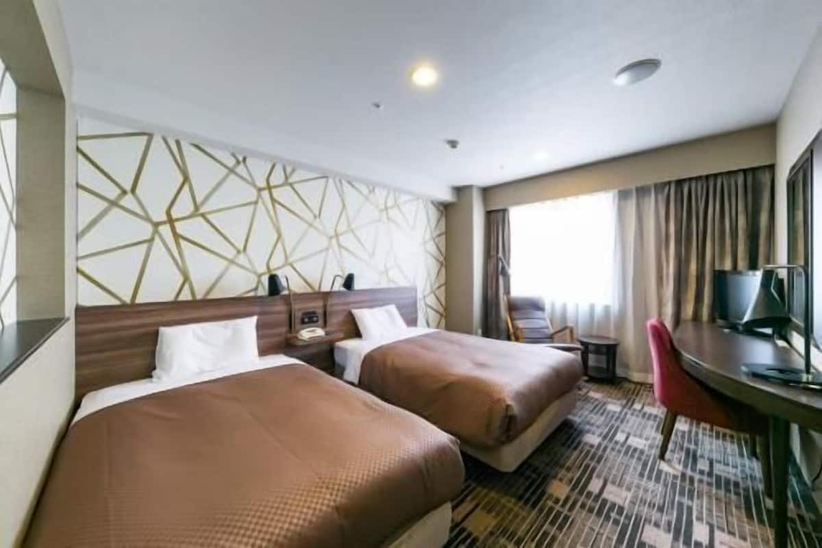 A hotel room with two beds, a desk, a chair, and a window with curtains.