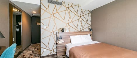 A hotel room with a bed, a desk, a chair, a wall with geometric patterns, and a ceiling light.