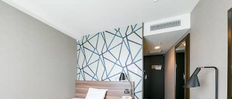 Une chambre d’hôtel avec un lit, une table de chevet, une lampe et un mur décoré d’un motif.
