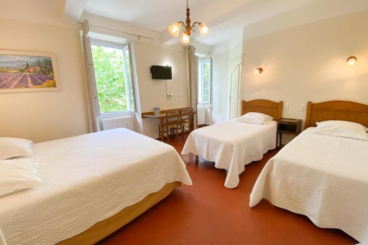 A hotel room with two beds, a dining table, a TV, and a painting on the wall.