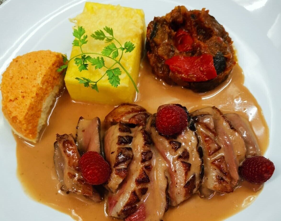 A plate with sliced duck breast, a side of mashed potatoes, and a bread roll.