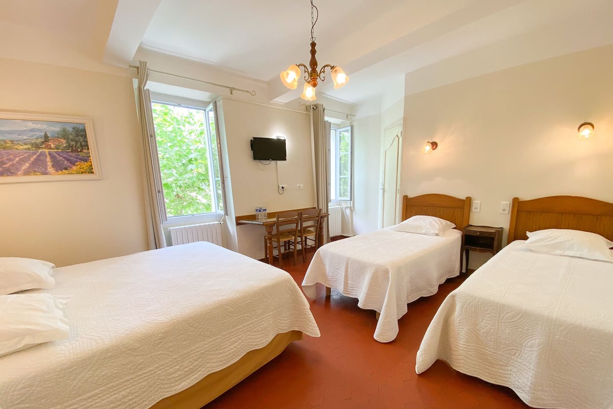 A hotel room with two beds, a desk, a chair, a television, and a painting on the wall.