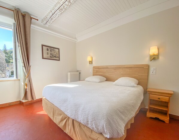 Una cama bien hecha con cabecera de madera, mesita de noche y lámpara de pared.