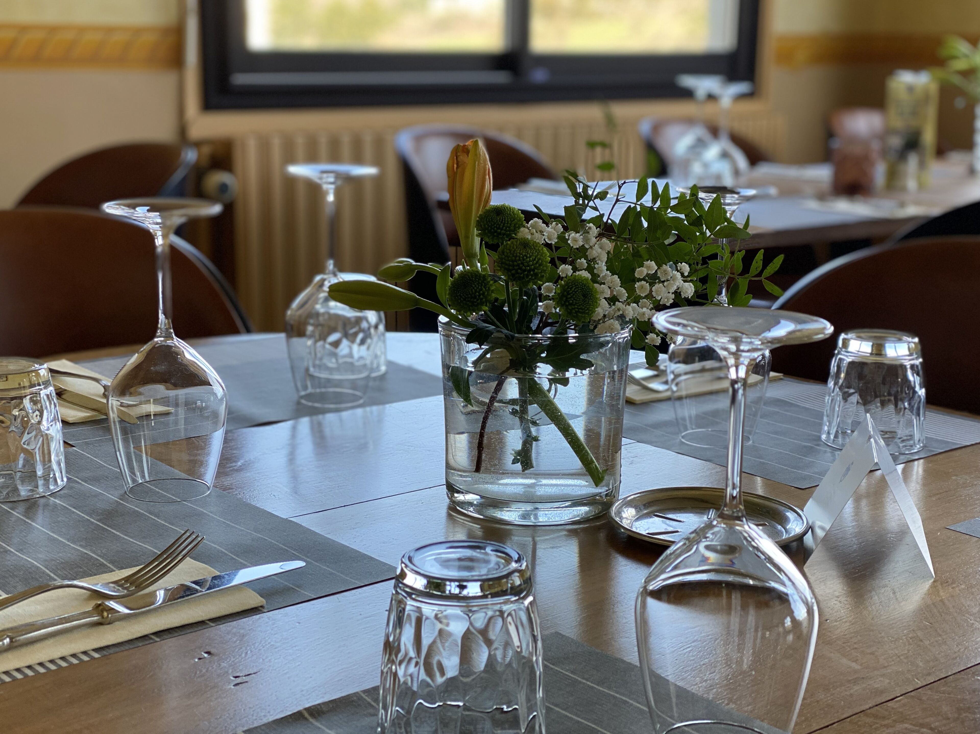 A dining table set with clear glassware, a vase with flowers, and a candle holder.