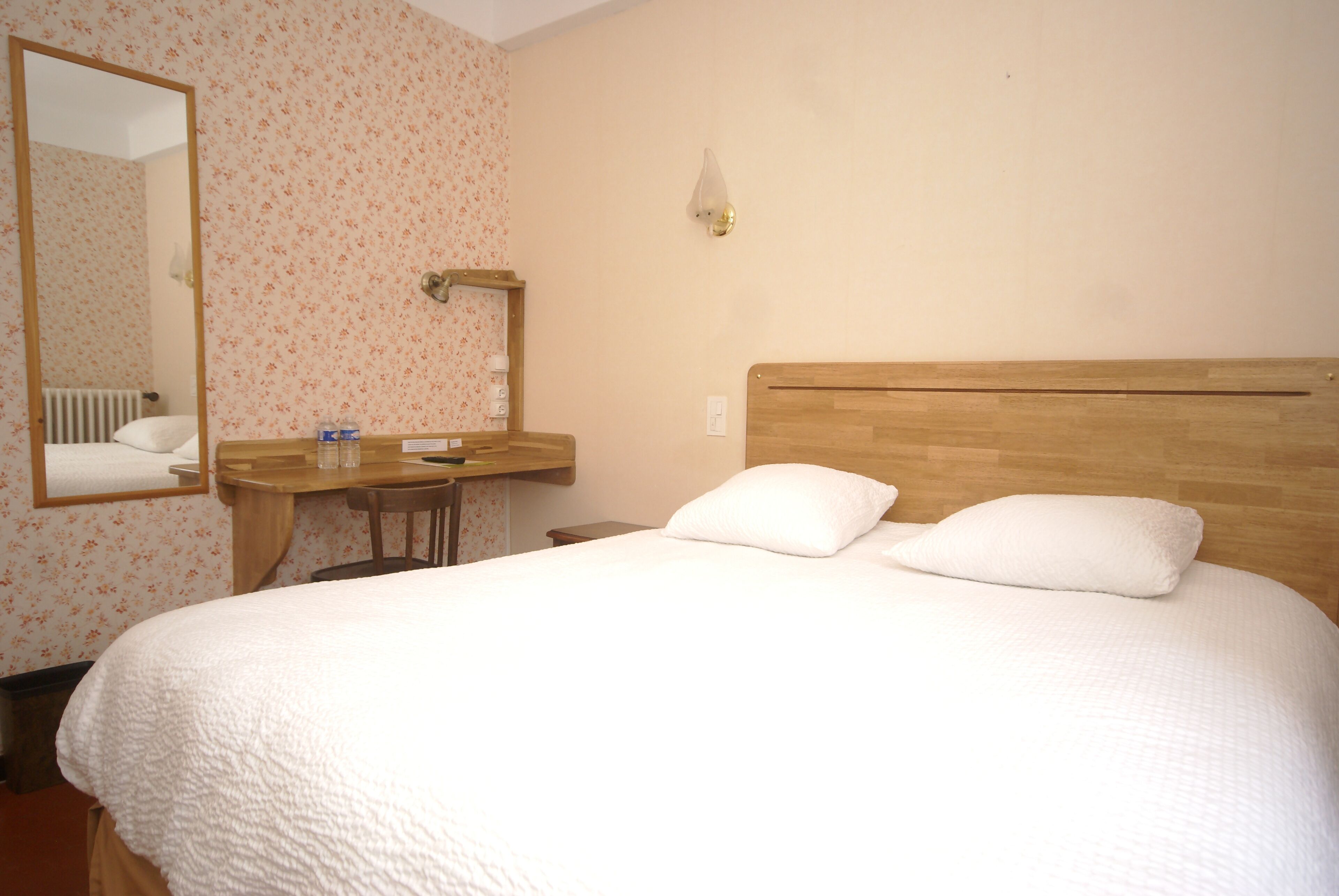 Een hotelkamer met een groot bed, een houten hoofdbord, een nachtkastje, een spiegel en een wandlamp.
