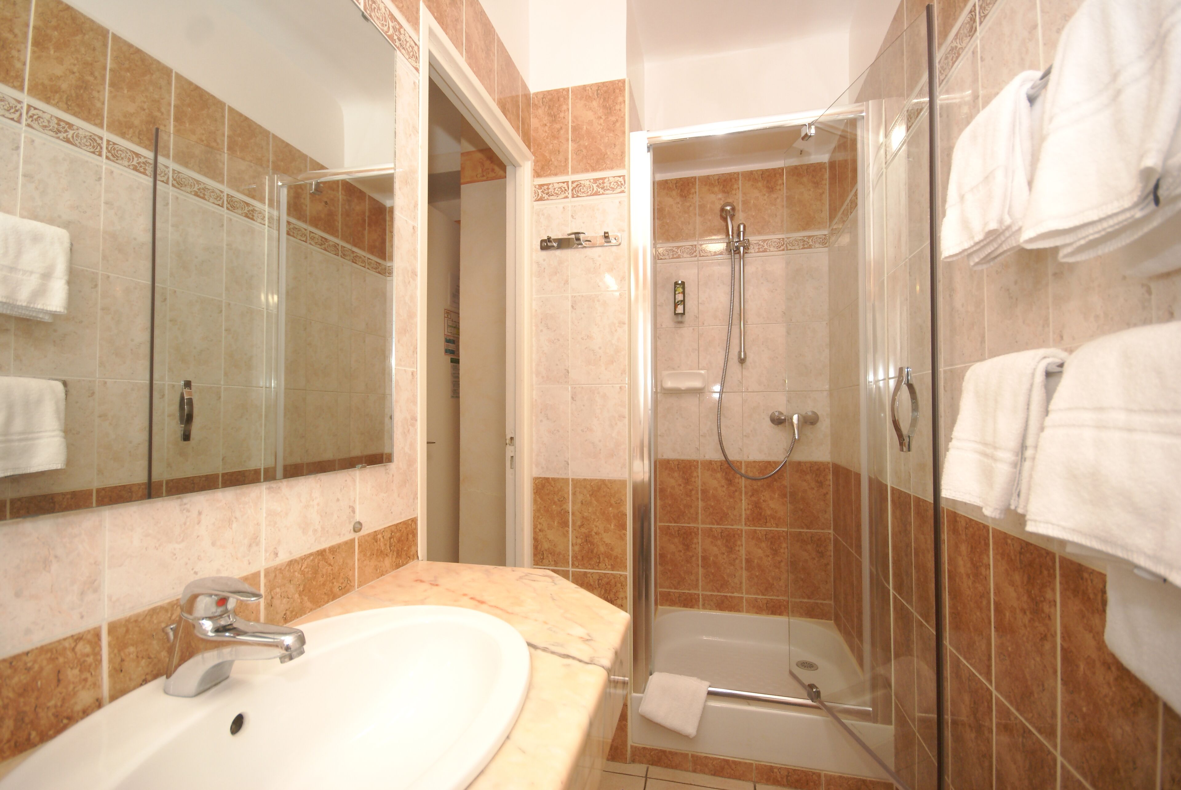 A bathroom with a sink, mirror, shower, and towels.