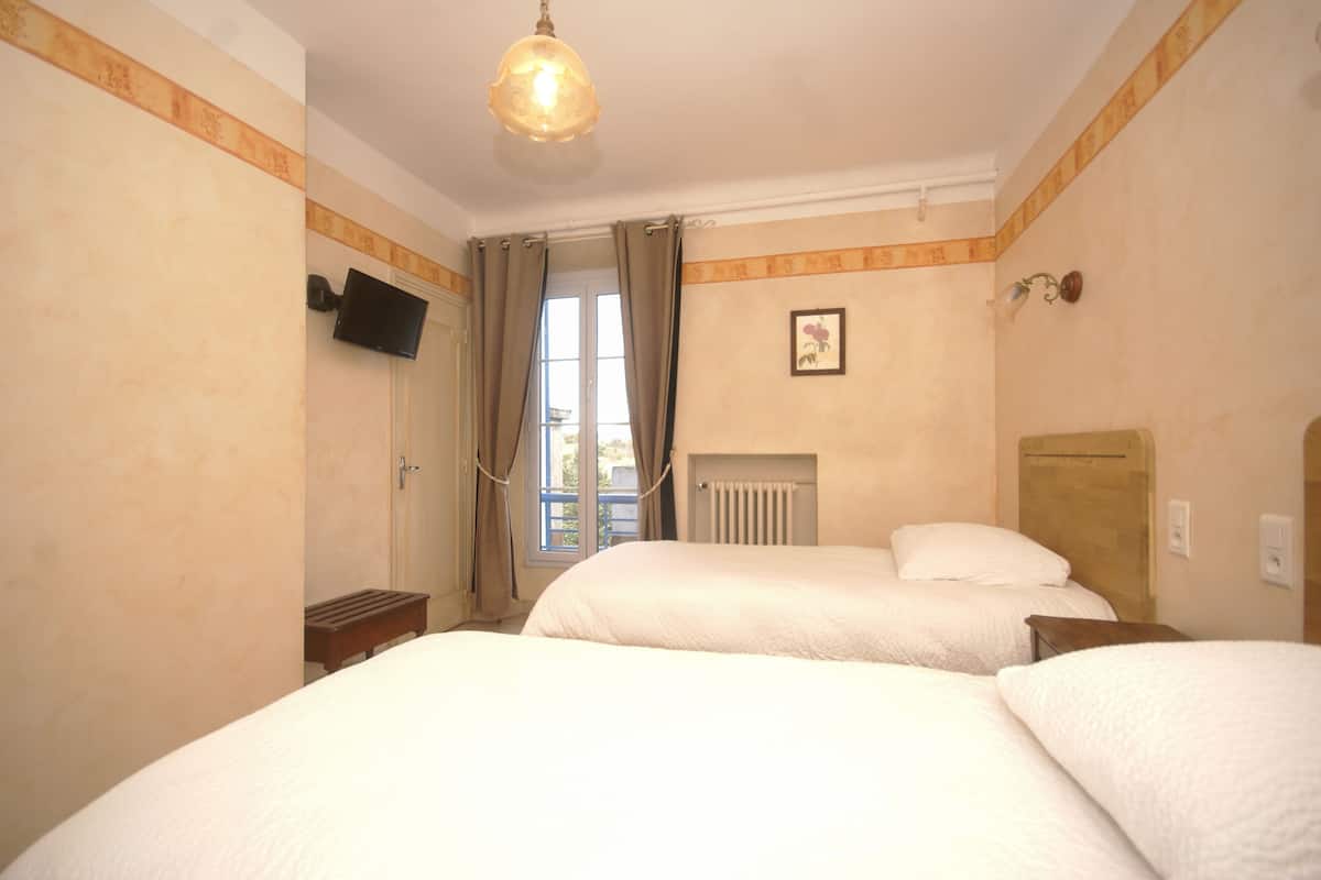 A hotel room with two beds, a television, a radiator, and a window with curtains.
