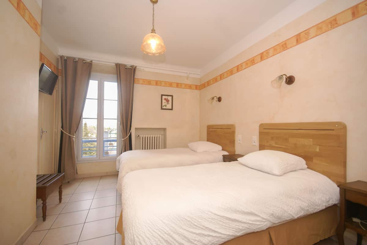 A hotel room with two beds, a television, a window with curtains, and a radiator.