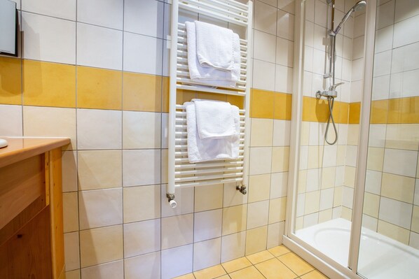 A bathroom with a shower, a towel rack with two towels, and a wooden counter. - Hôtel Les Bruyères (Morzine)