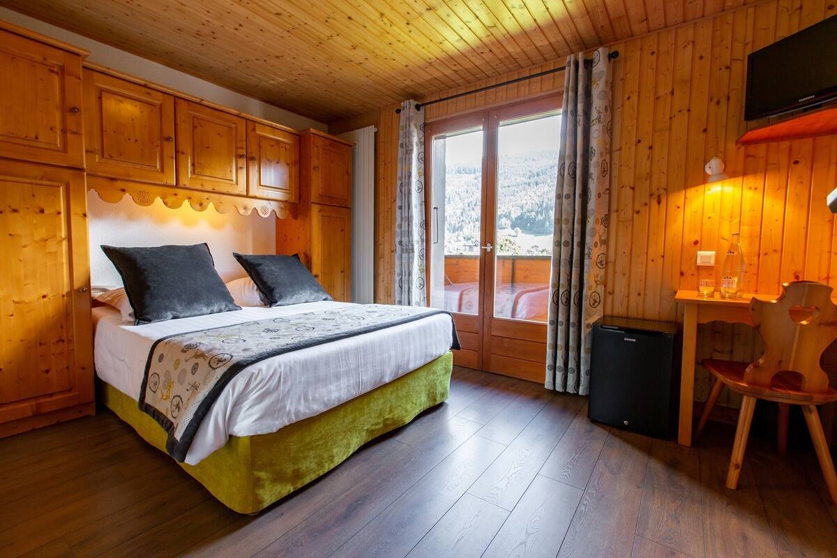 Ein Zimmer in einer Holzhütte mit einem Bett, einem Schreibtisch und einem kleinen Kühlschrank.