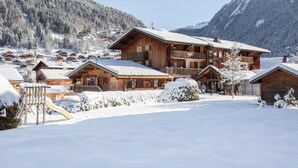 Una cabaña de madera con varios balcones y una pista de esquí en una zona montañosa nevada.