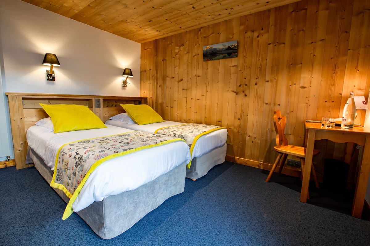 Ein Zimmer mit zwei Betten, Holzwänden, einem Schreibtisch und zwei Wandleuchten.