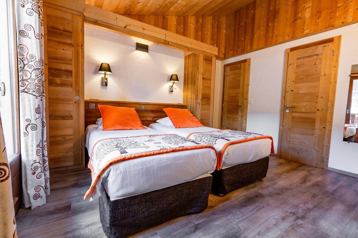 Ein Zimmer mit Holzwandverkleidung, einem Doppelbett, zwei Nachttischlampen und einer Tür mit Spiegel.