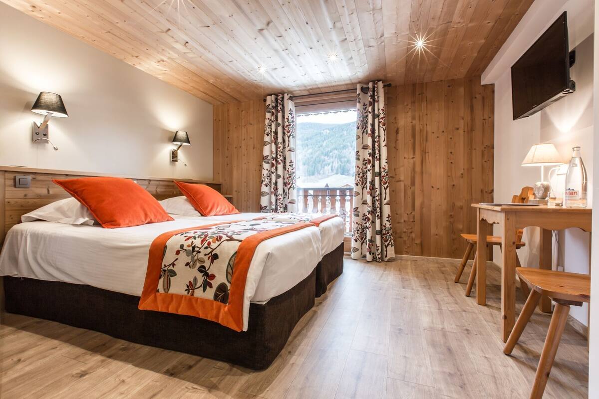 Ein Zimmer mit Holzwänden, einem Bett, einem Schreibtisch und einem Fernseher.