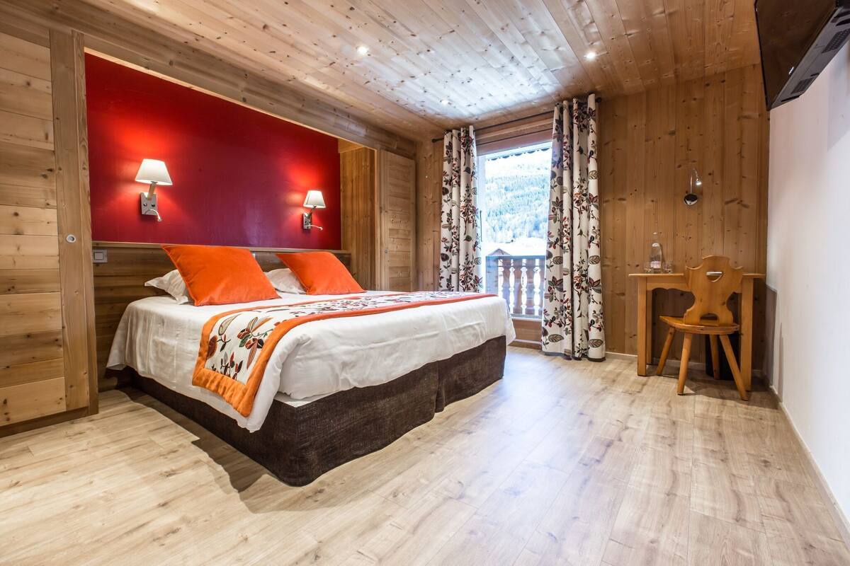 Ein Schlafzimmer mit Holzwänden, einem Bett, zwei Wandlampen, einem Holzstuhl und einem Fenster mit Vorhängen.