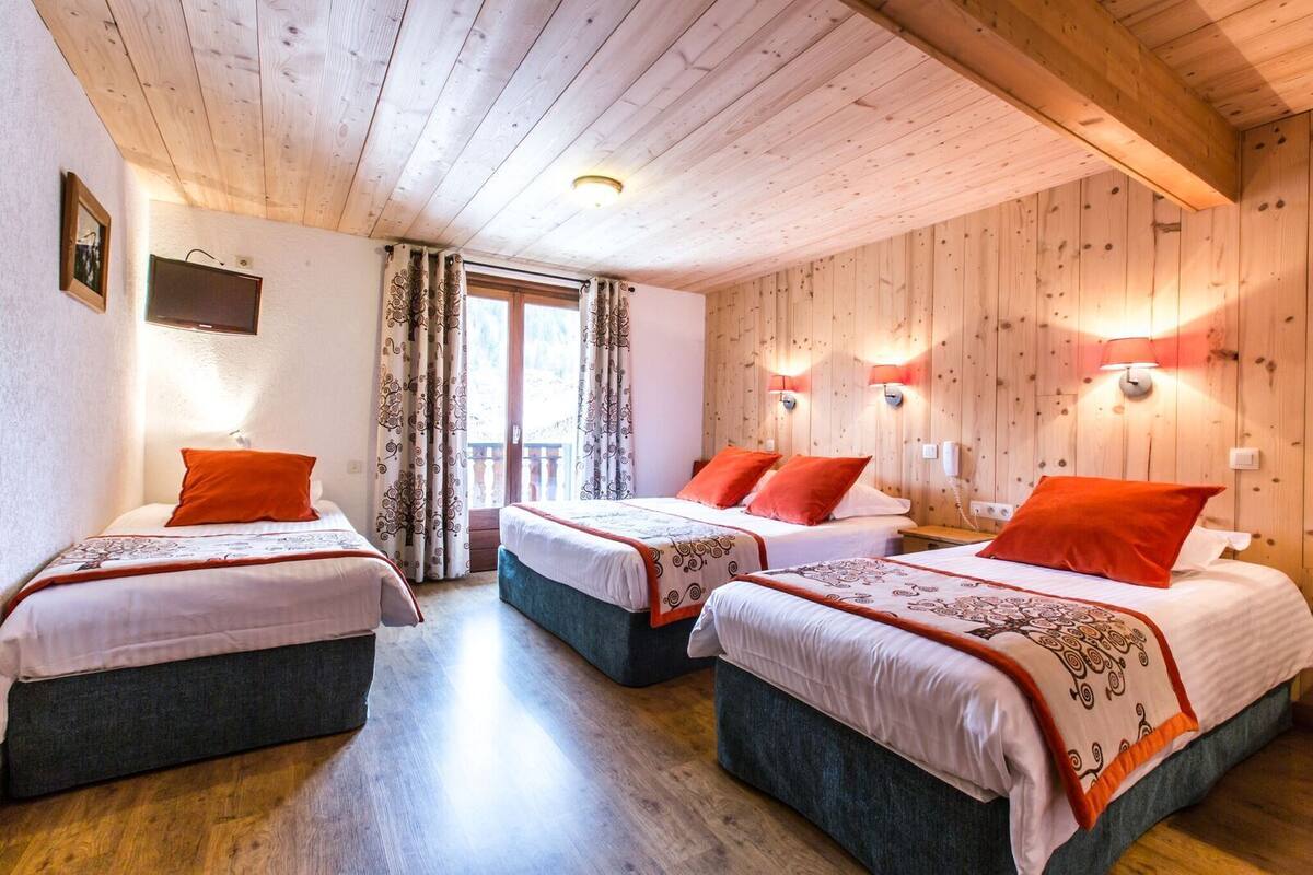Ein Zimmer mit drei Betten, Holzwänden und einem Balkon.