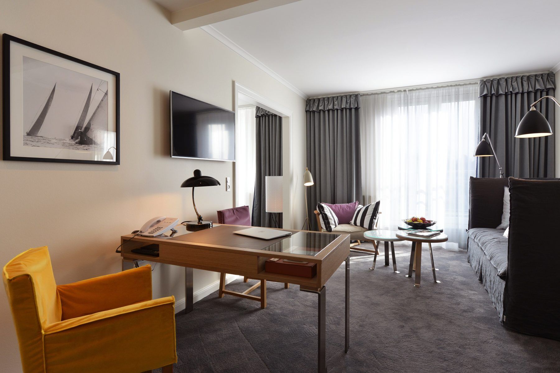 A hotel room with a desk, chair, bed, and a TV on the wall.