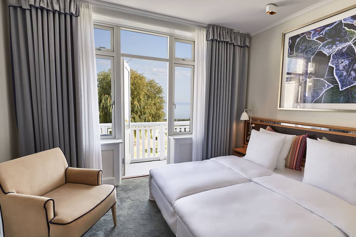 Un cuarto de hotel con cama, sofá, un ventanal con cortinas, vista al exterior y un cuadro en la pared.