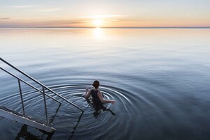 Una persona de pie en un muelle que se adentra en aguas tranquilas, con un atardecer de fondo.