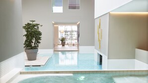 Una piscina interior moderna con agua cristalina, una planta en maceta y vistas de la ciudad a través de amplios ventanales.
