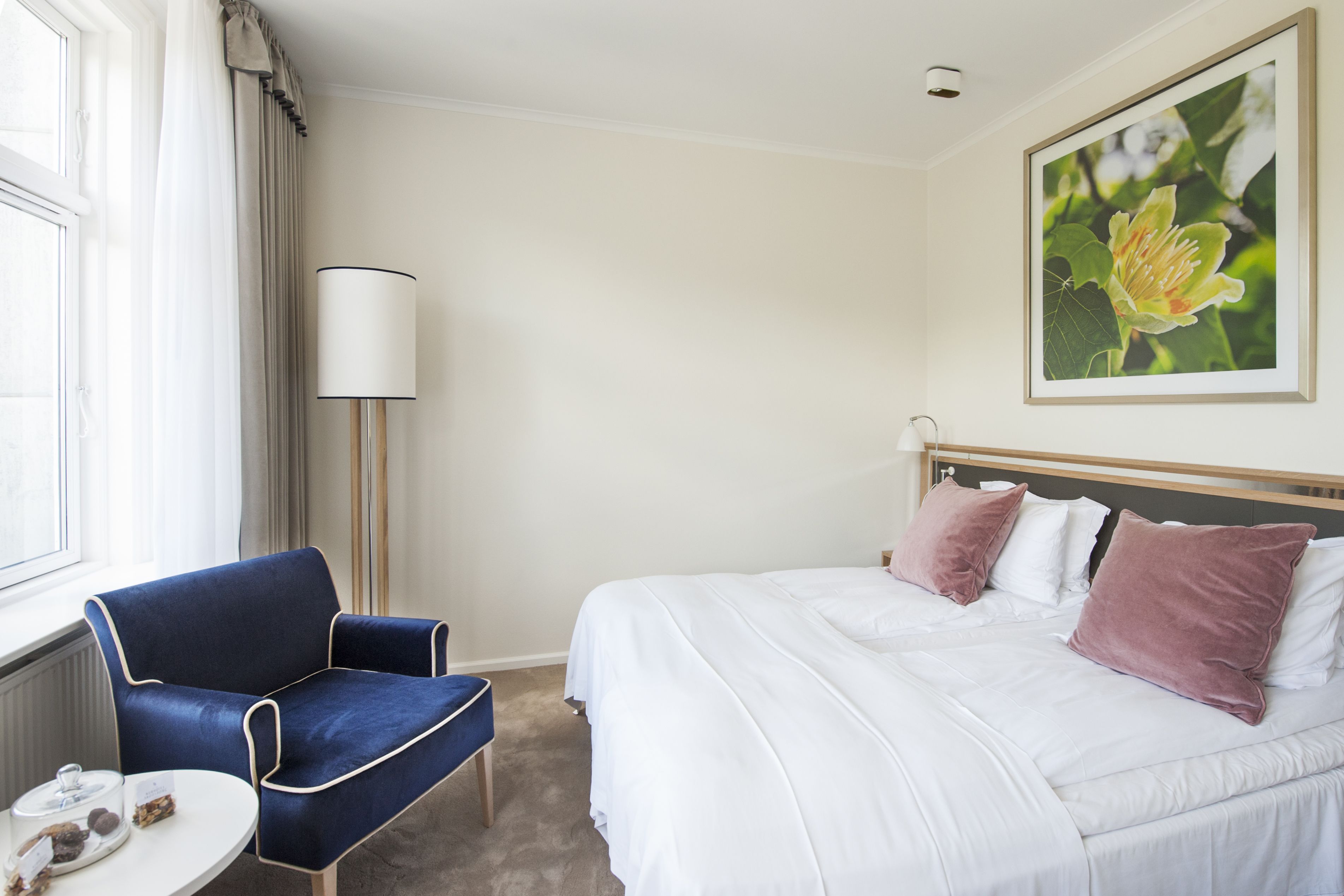A hotel room with a bed, a chair, a lamp, and a window.