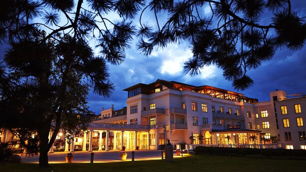 Un hotel grande de varios pisos con una entrada bien iluminada y un césped cuidado.