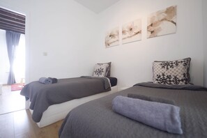 Una habitación con dos camas, cada una con una manta y almohada grises, un tapete rojo y tres obras de arte floral abstractas en la pared.