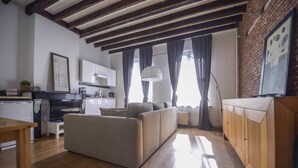 Una sala de estar moderna con sofá, piso de madera y una zona de cocina con armarios y electrodomésticos.