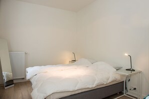 Un dormitorio con cama, mesitas de noche, espejo y radiador.