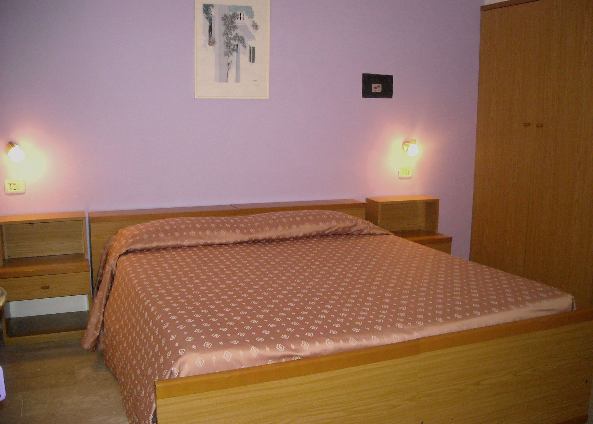 Ein Schlafzimmer mit einem Bett, zwei Nachttischen, einem Kleiderschrank und zwei Wandlampen.