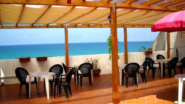 An outdoor patio with wooden pergola, black plastic chairs, and tables, overlooking the sea. - Diavin (Vibo Valentia)